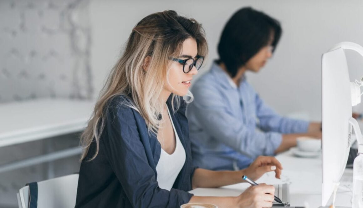Busy female freelancer with long hair working with tablet and drinking coffee. Indoor portrait of concentrated japanese student using computer in classroom..